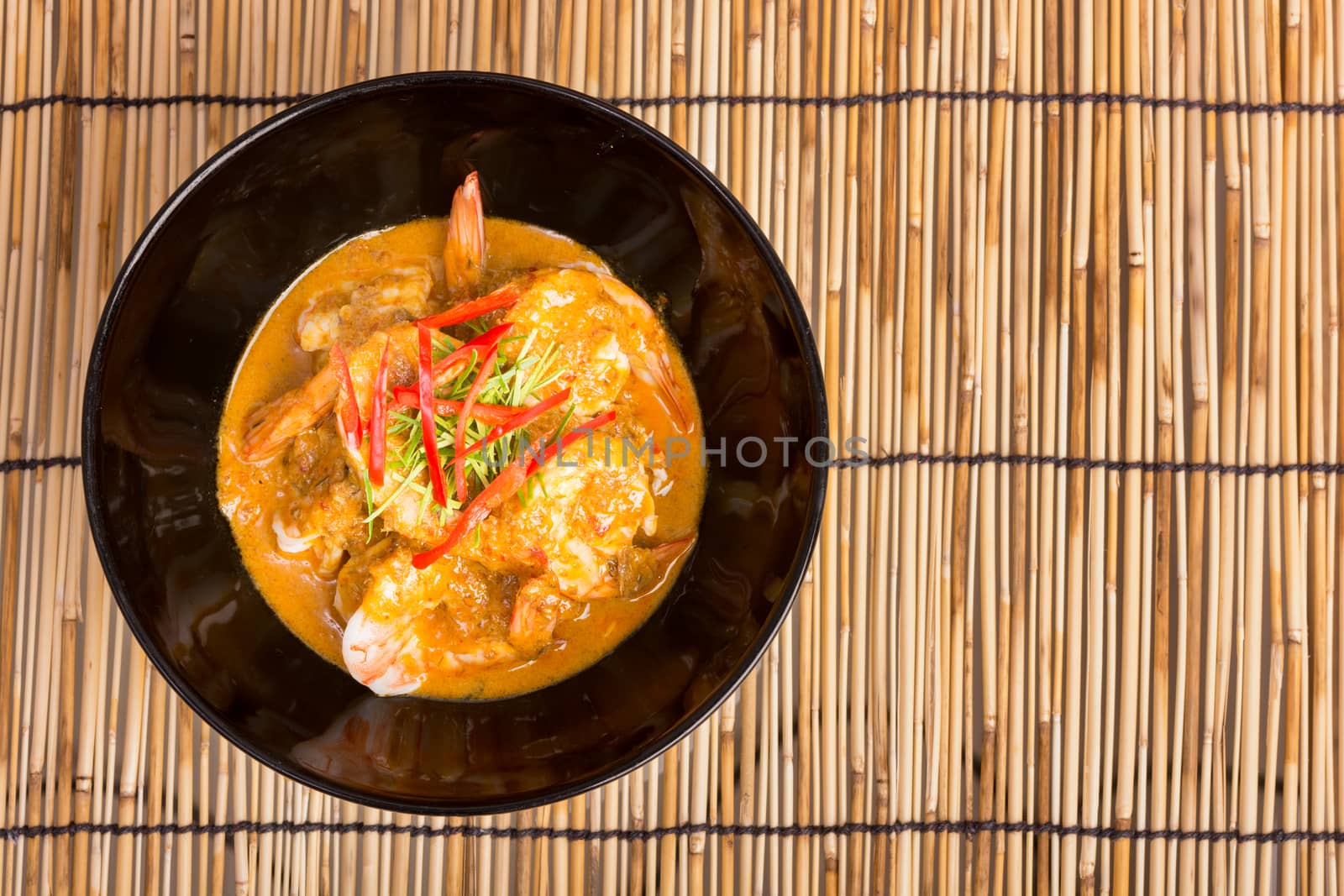 Curry fried shrimps in black cup closeup on table with wooden background