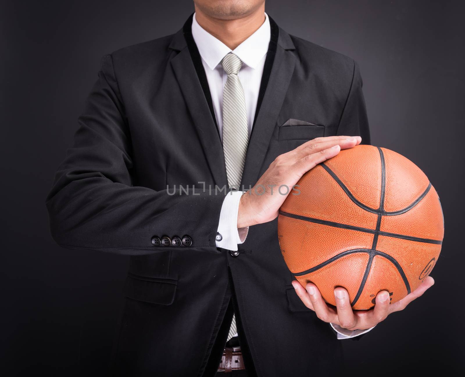 Young businessman holding basketball ball isolated on black background