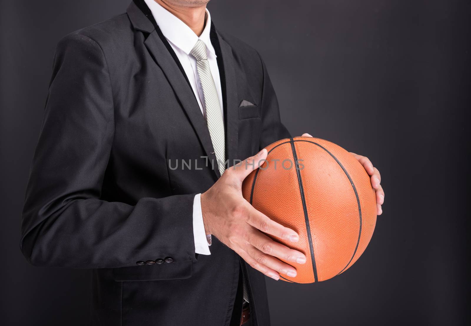 Young businessman holding basketball ball isolated on black background