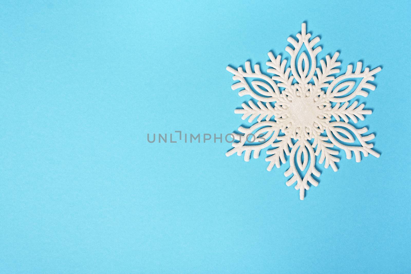 White glittery snowflake on pastel blue background by Mendelex