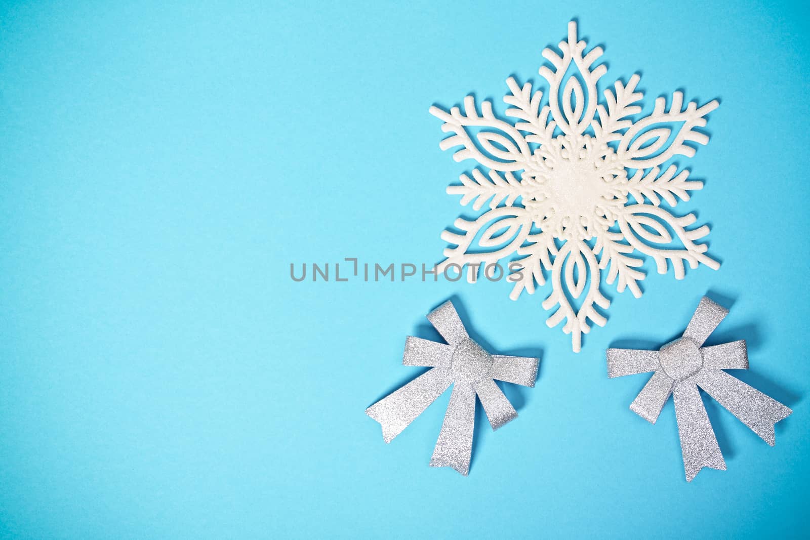 White glittery snowflake and bows on pastel blue background by Mendelex