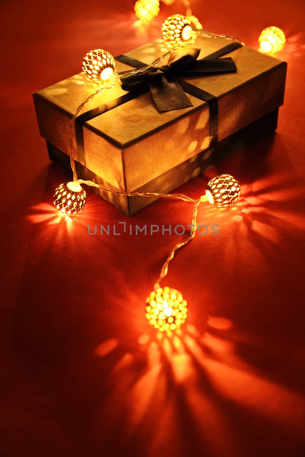 Wrapped gift under glowing Christmas lights by Mendelex