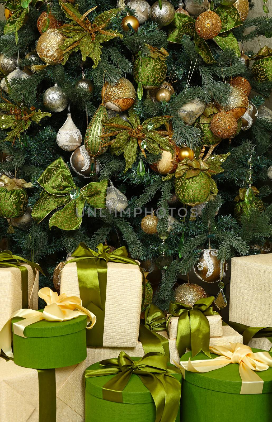 Close up green and beige paper wrapped gift boxes with ribbon bows under decorated Christmas tree, high angle front view
