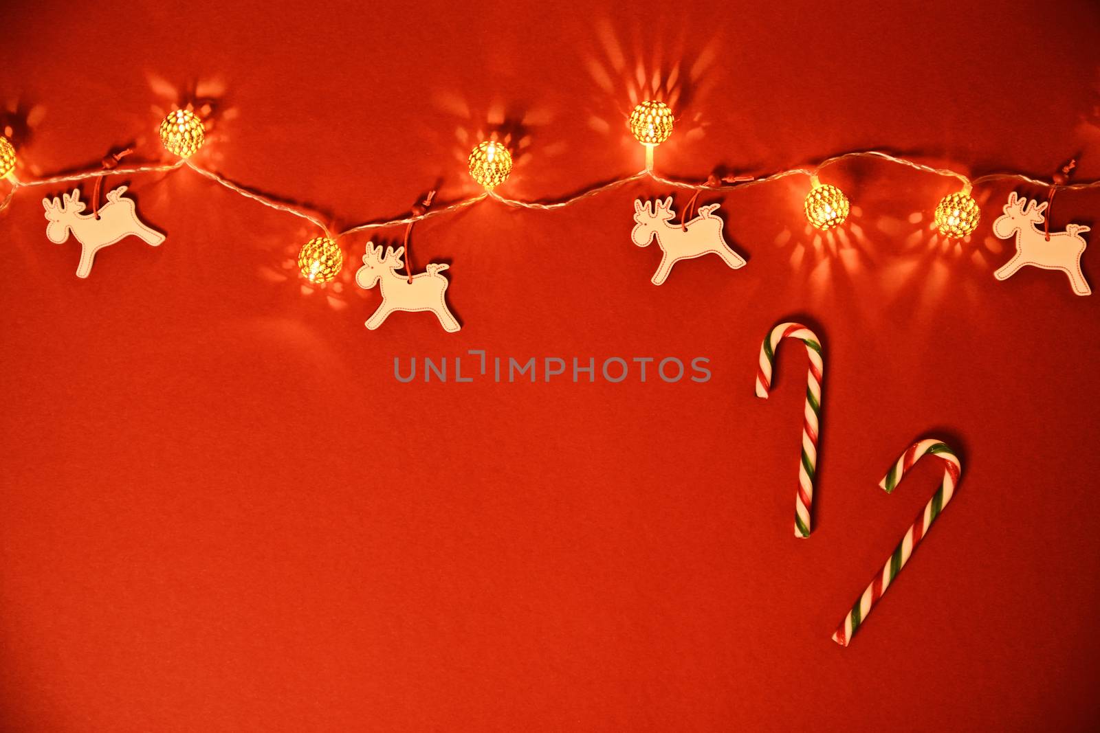Christmas and New Year composition. Seasonal greeting card concept with white Christmas lights, reindeers and candy cane on red background. Christmas, winter, new year concept. Flat lay, top view, copy space. 