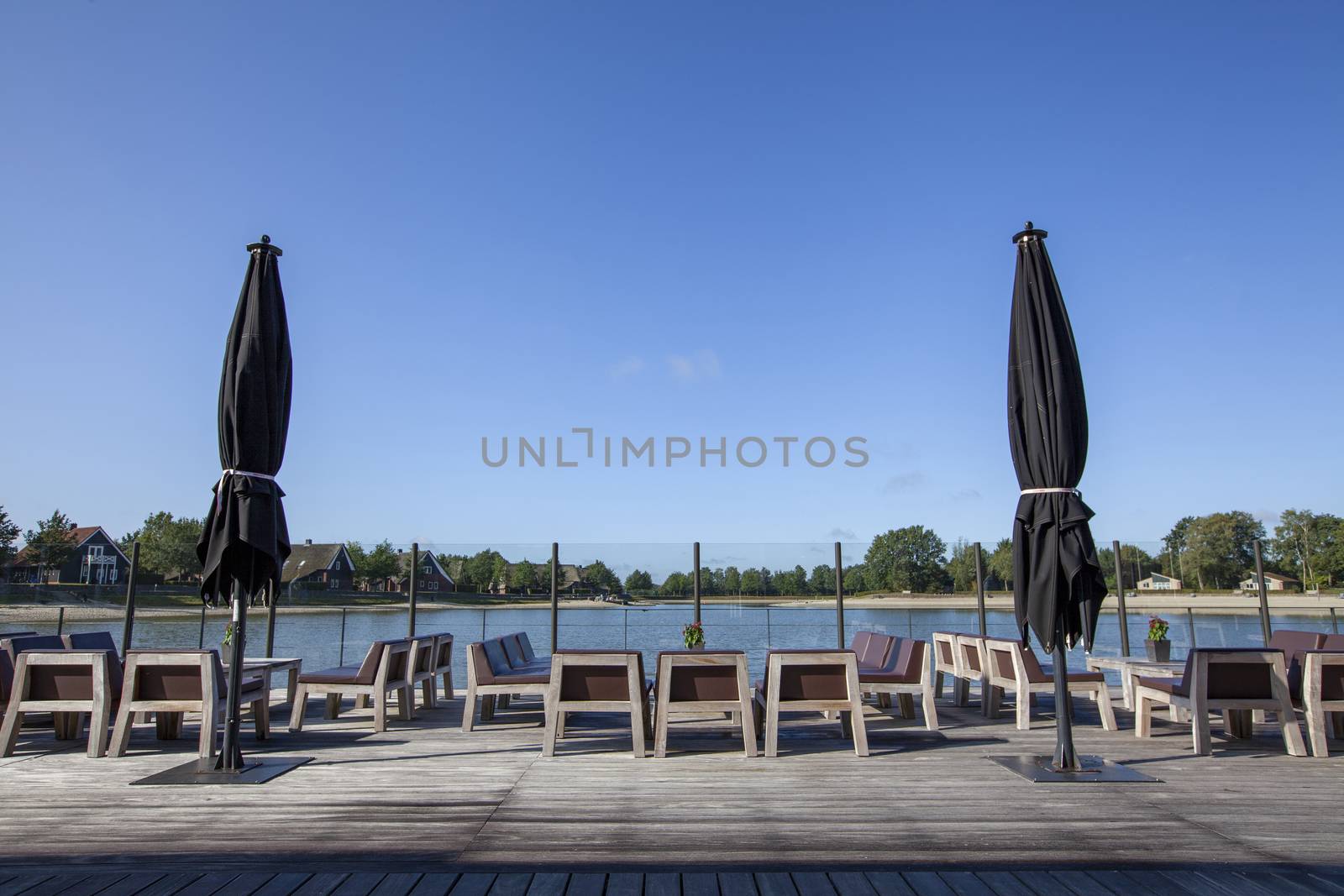 beach chair and black umbrella on the floor with lake view and a blue sky