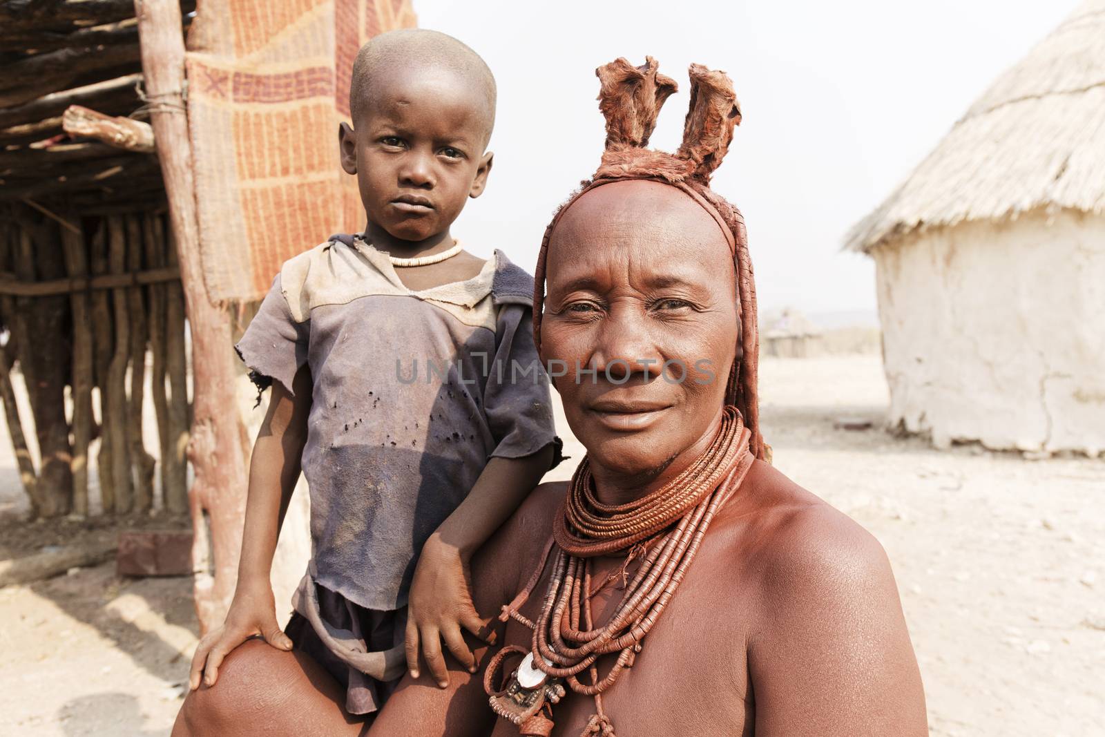 Himba woman with her small son smiling to the camera in the village of Himba people