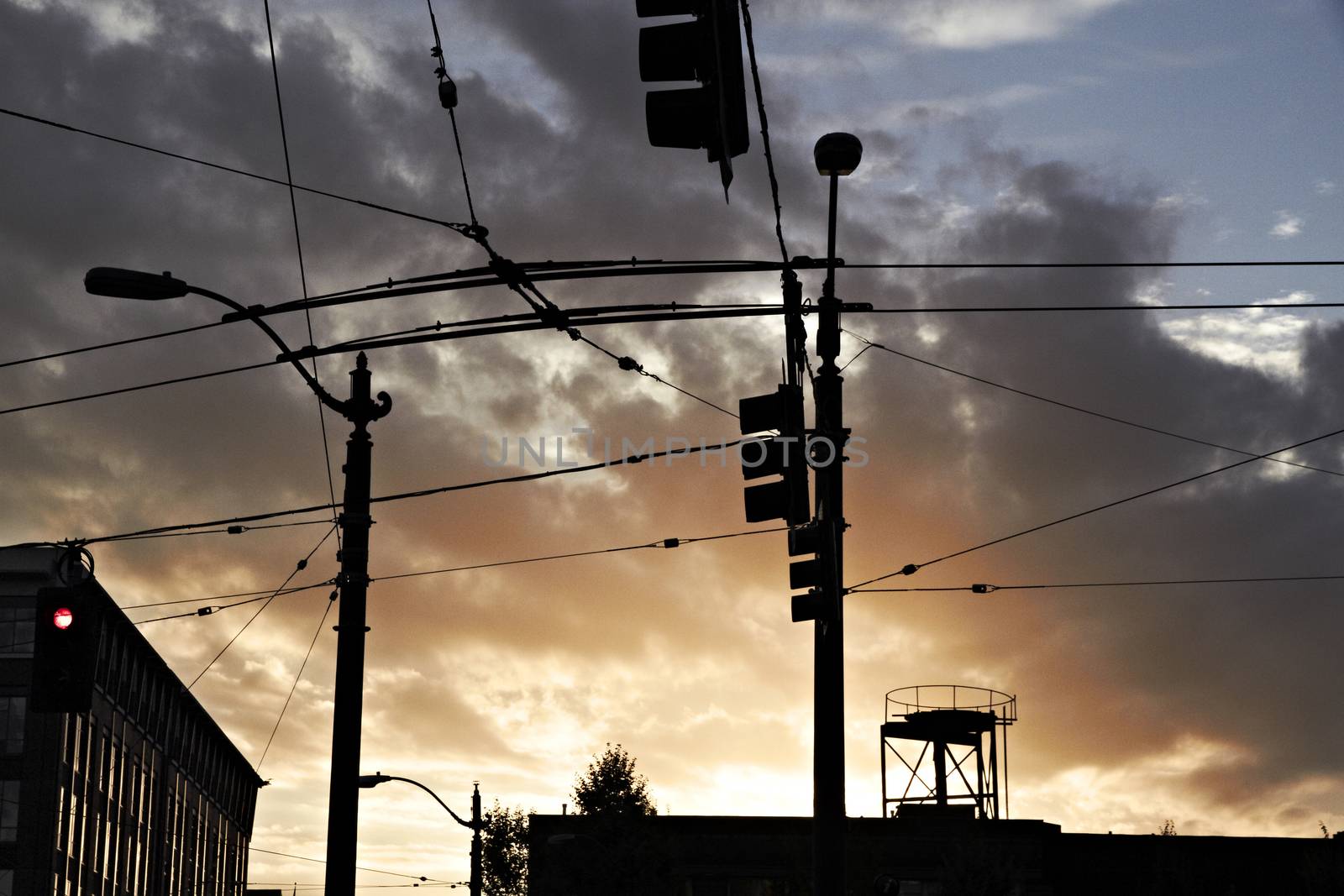 High-voltage electricity wires and traffic lights silhouetted against sunset.