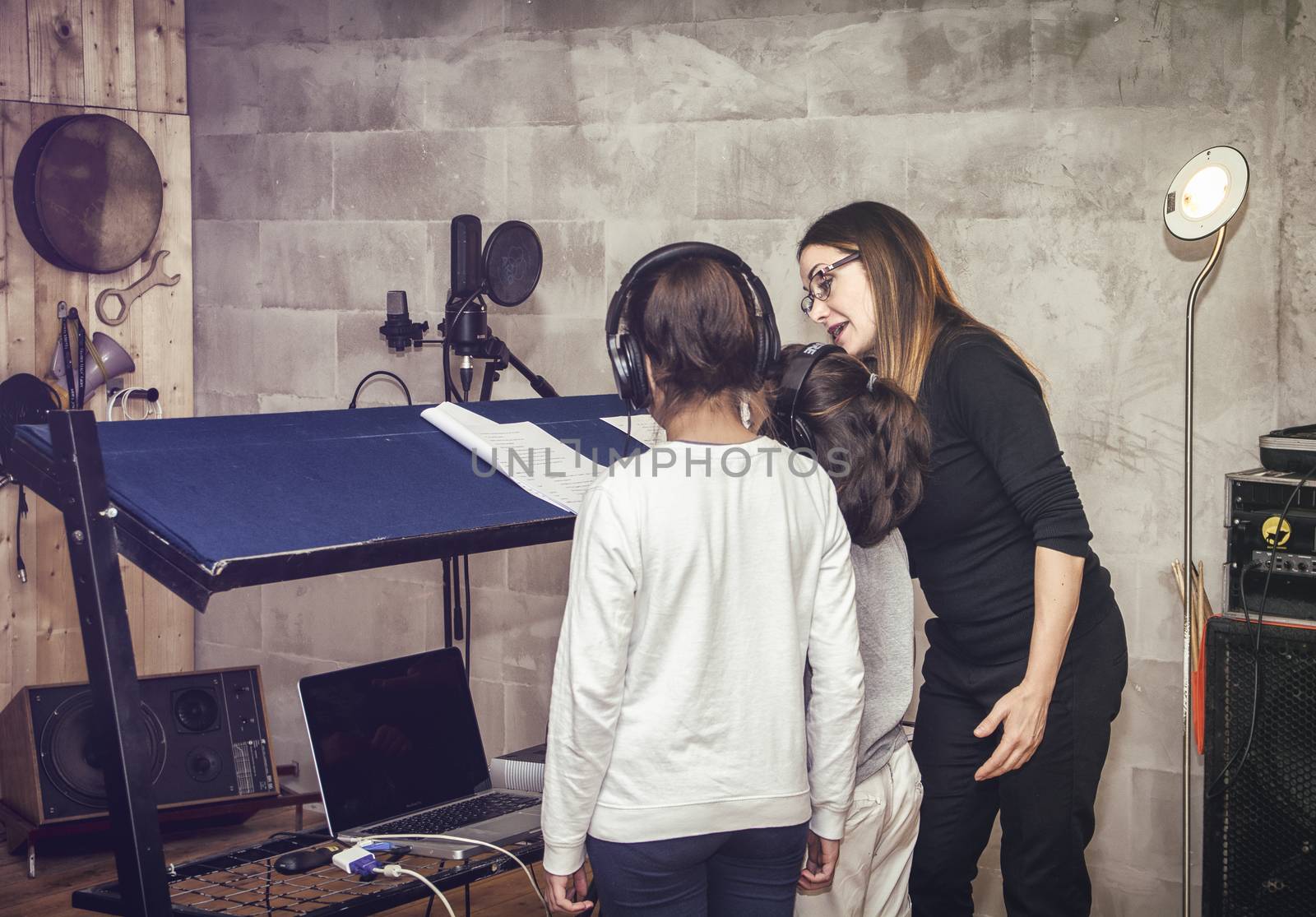 Rear view of two unrecognizable children in headphones with female acting or singing teacher in recording studio