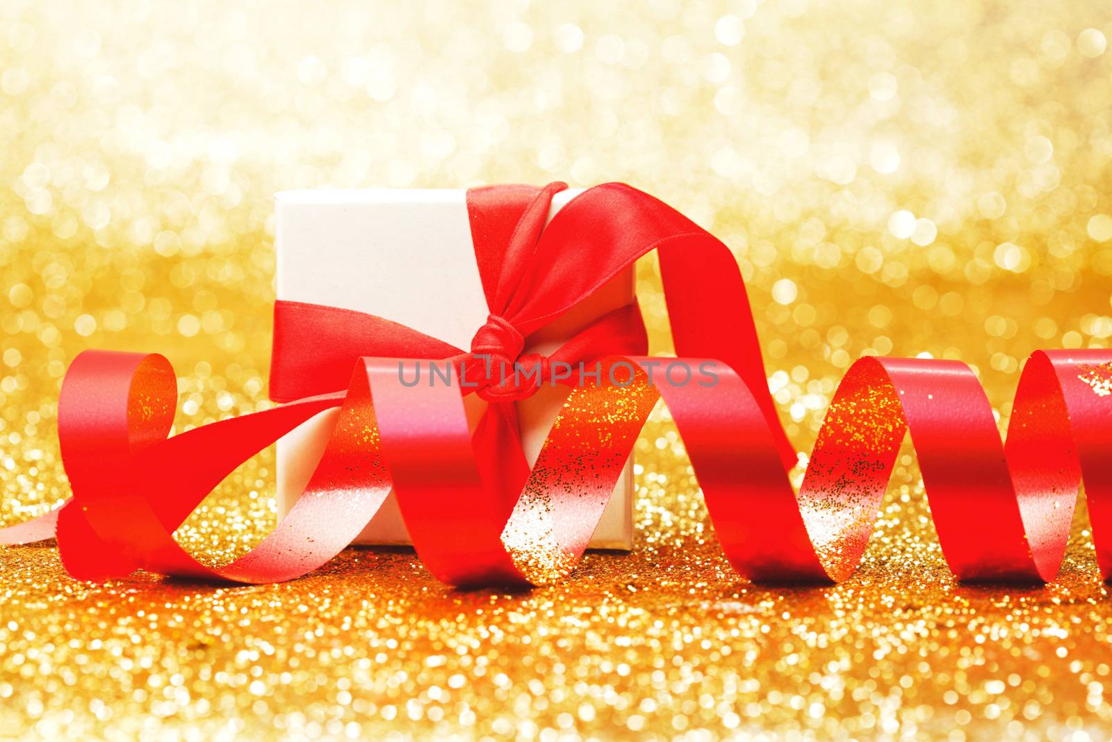 White gift box with red ribbon bow on golden glitter background