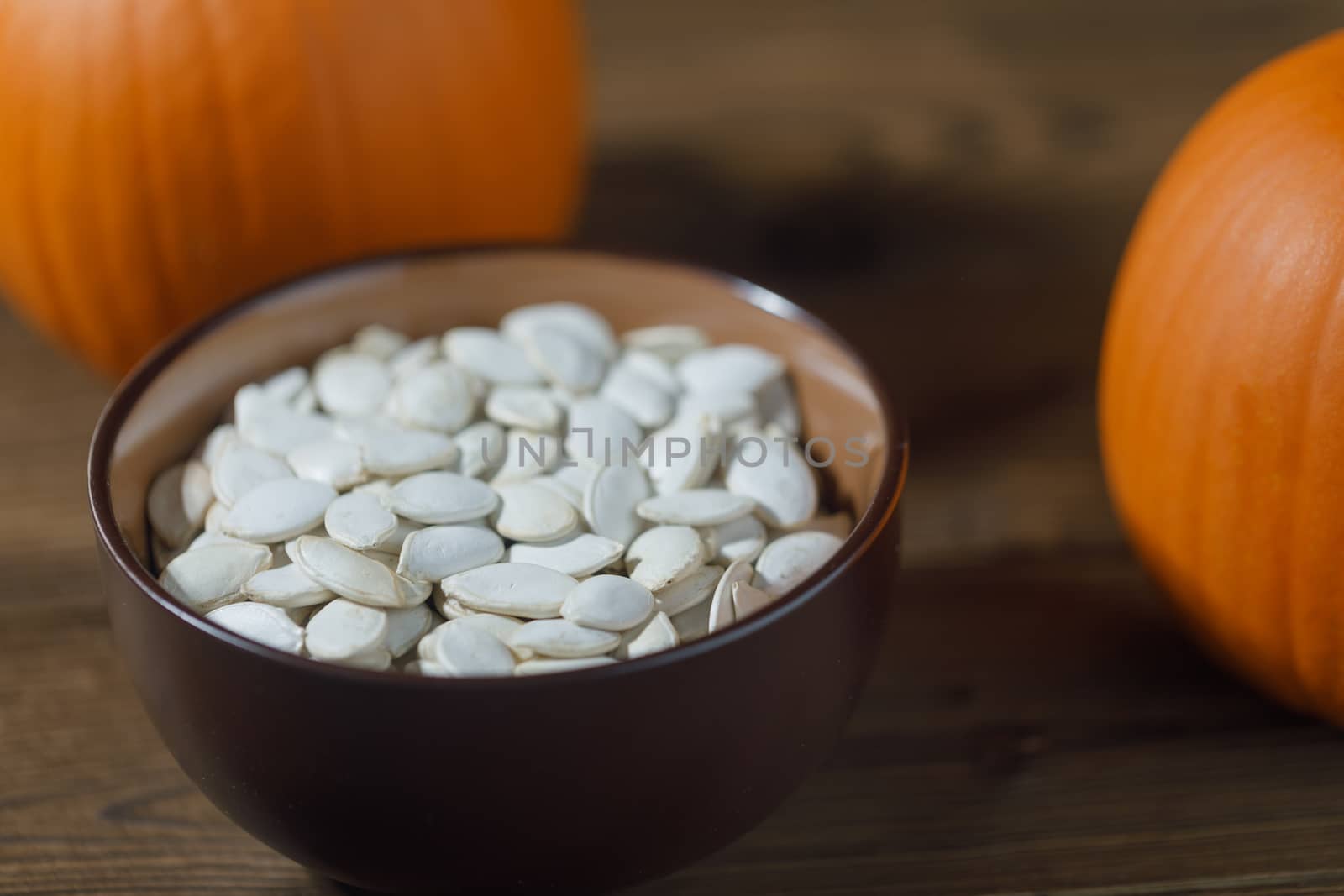 Fresh orange pumpkins and pimpkin seeds in a bowl close-up on wooden background