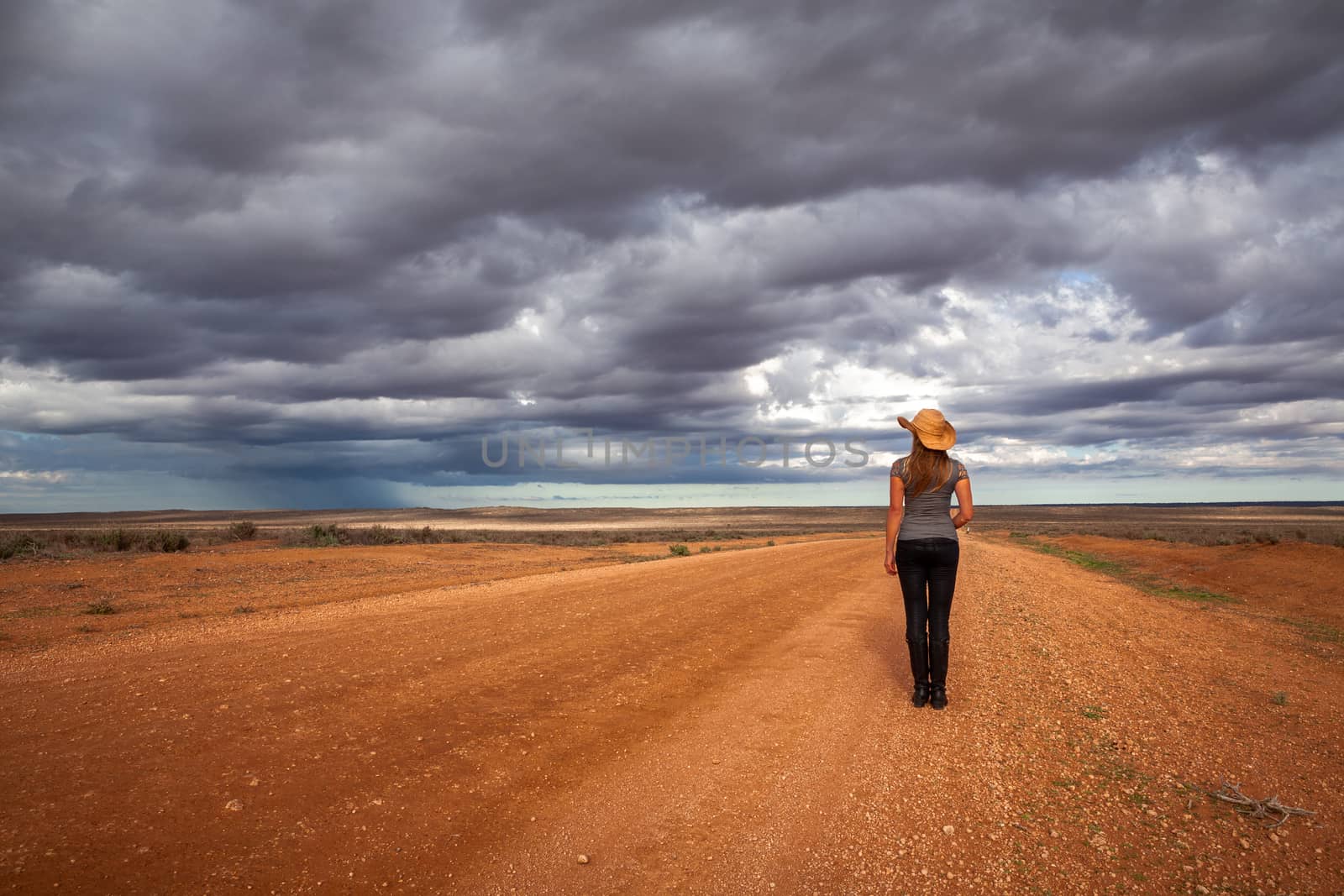 Farm girl watches the storm over an arid desert landscape of outback Australia