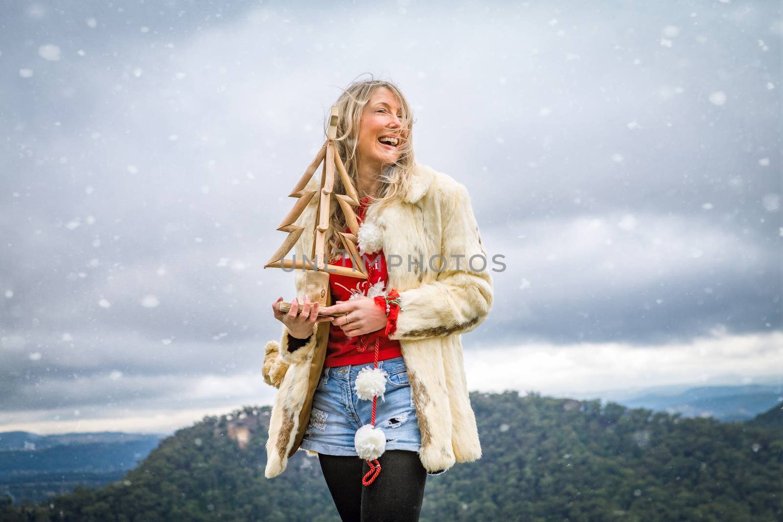 A woman holds wooden Christmas tree outdoors in the mountains, with snow falling.  Christmas in Blue Mountains, Christmas in July or seasonal concept