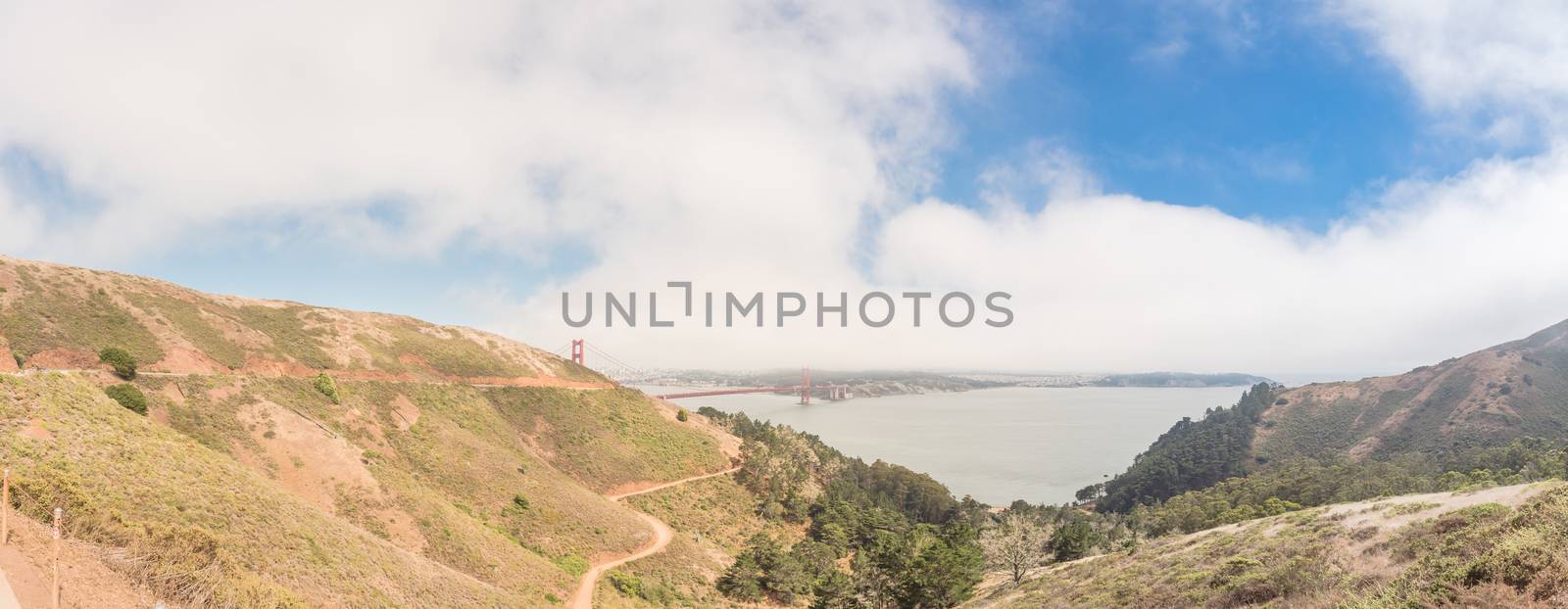 View from Golden Gate Observation Deck to the red bridge and downtown San Francisco in foggy summer day. Panorama ocean view near Hawk Hill with steep hillside road and open bay.