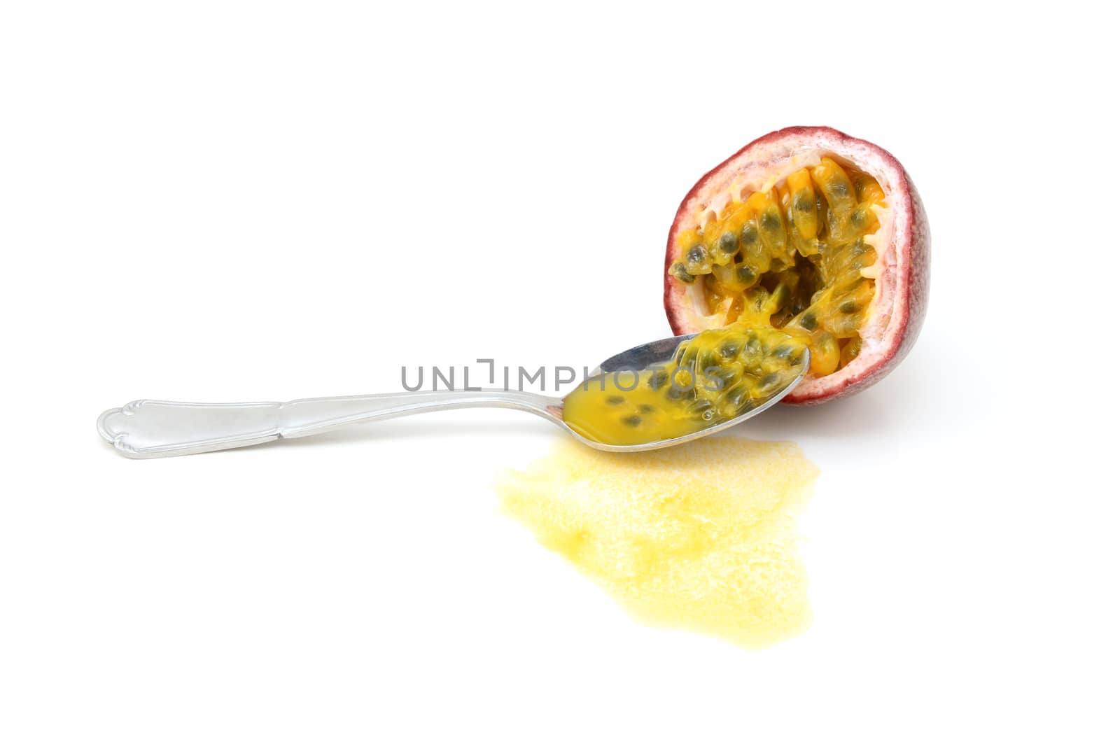 Spoon scooping out seeds from half a purple passion fruit with sweet spilled juice, on a white background