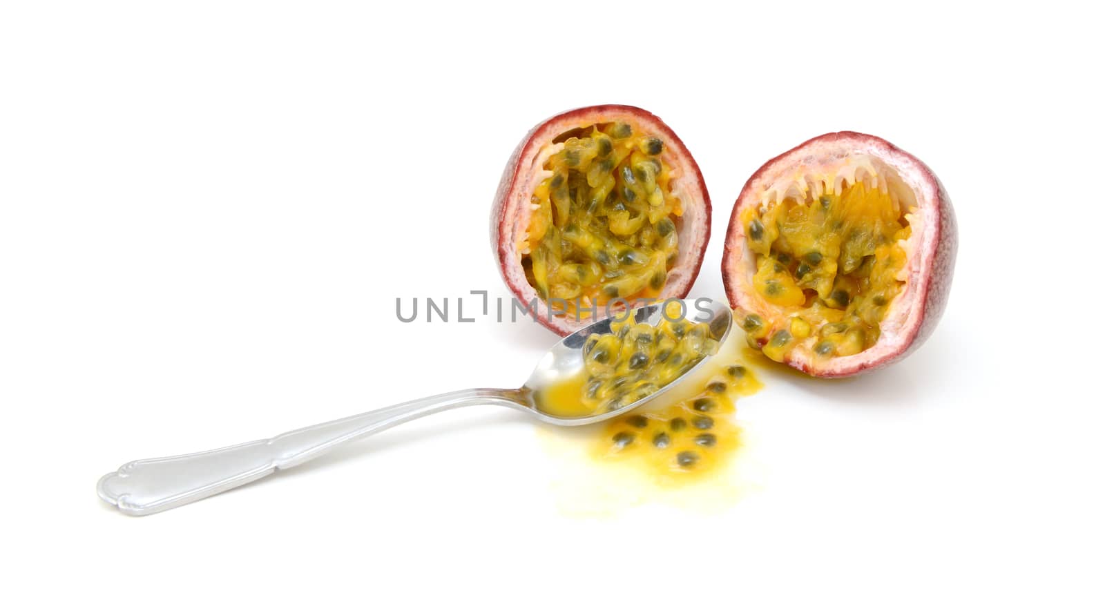 Spoon scooping out pulp and seeds from a purple passion fruit cut in half, on a white background