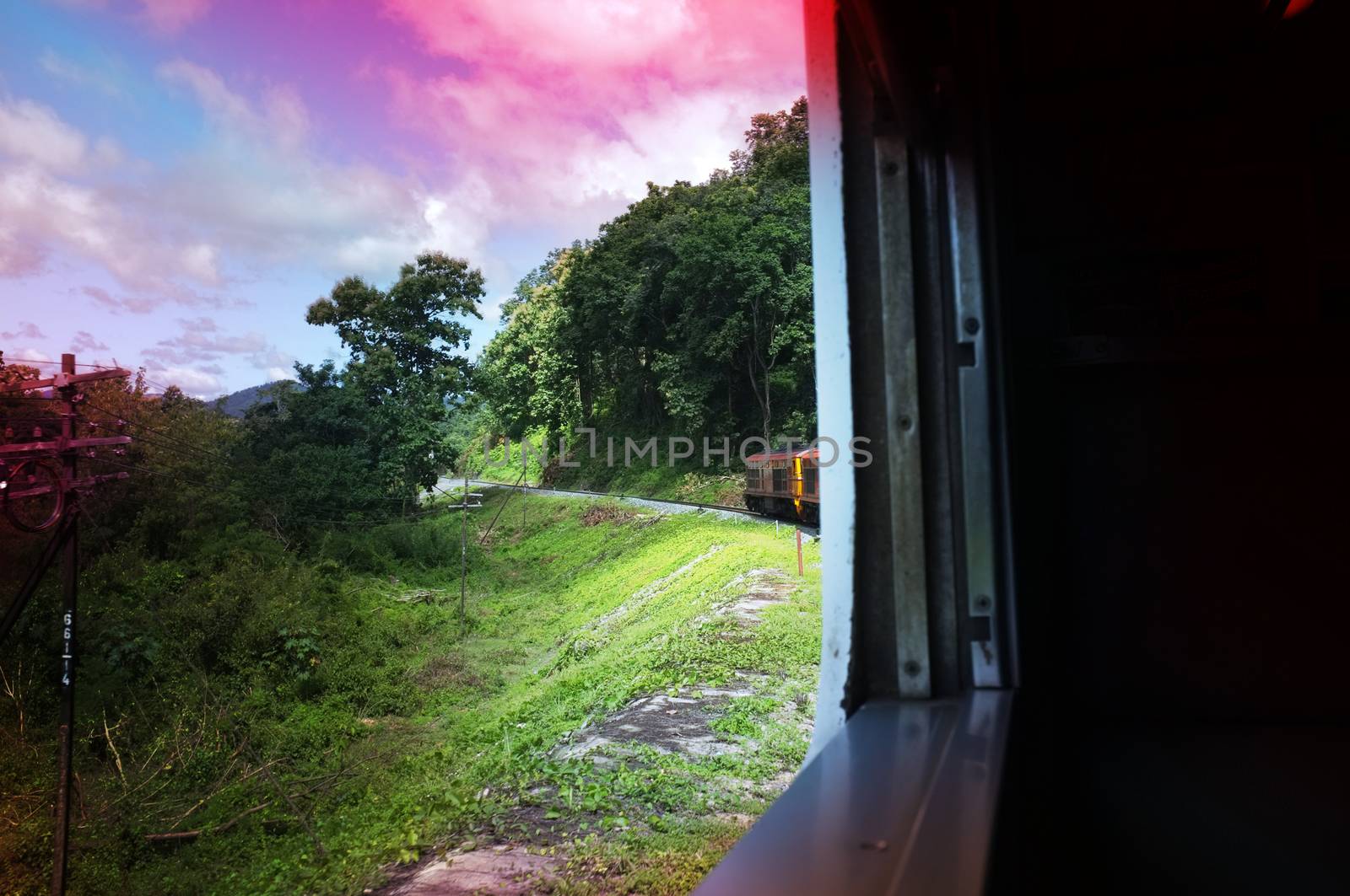 View from train railway makes a curve bend through beautiful natural green grasslands and mountains . Travel in Thailand , Effect saturation