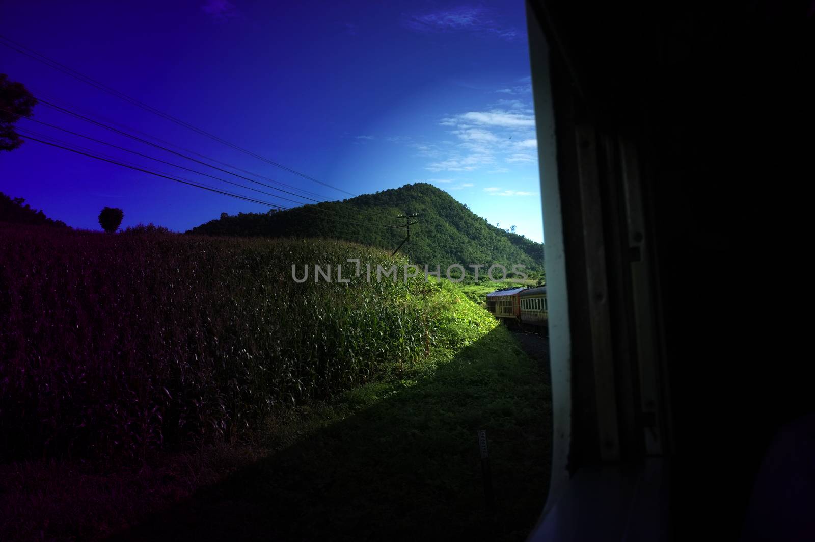 View from train railway makes a curve bend through beautiful natural green grasslands and mountains . Travel in Thailand ,Effect saturation