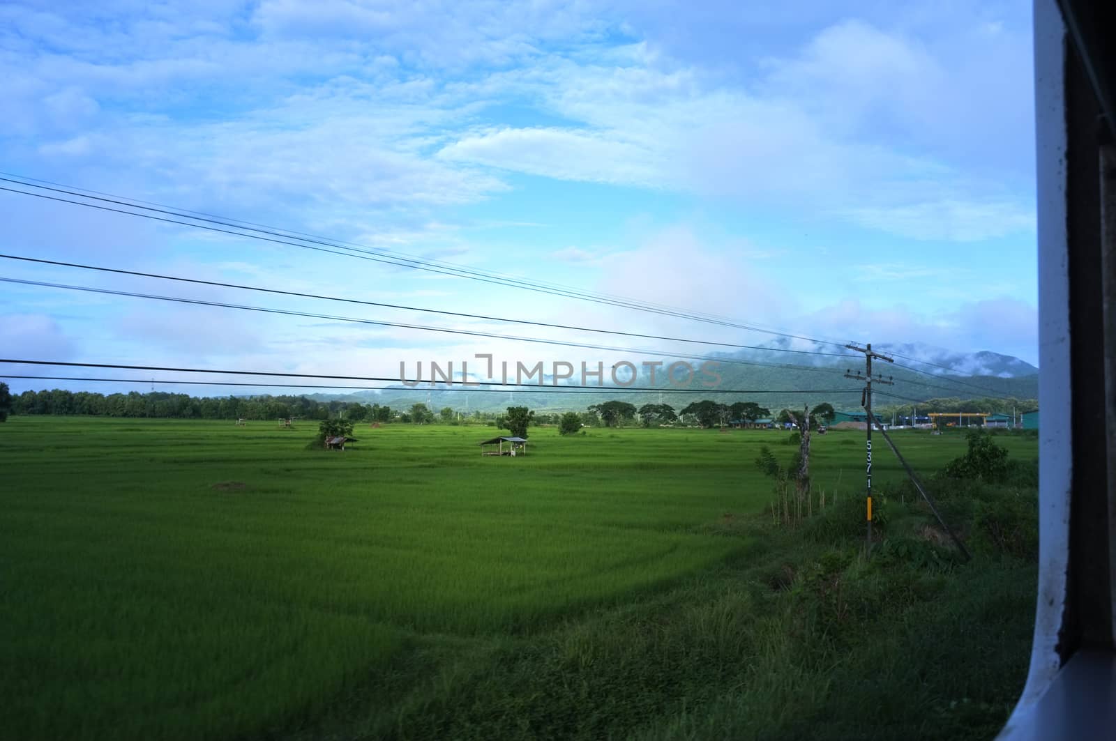 View from train window in motion of countryside and sky on sunny warm , in Thailand , 