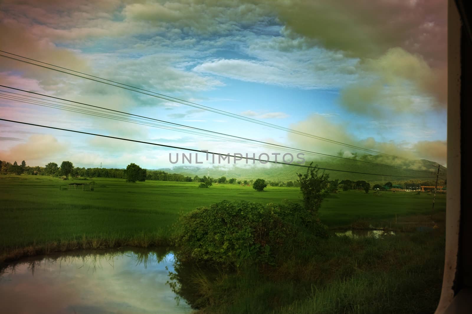 View from train window in motion of countryside and sky on sunny warm , in Thailand , 