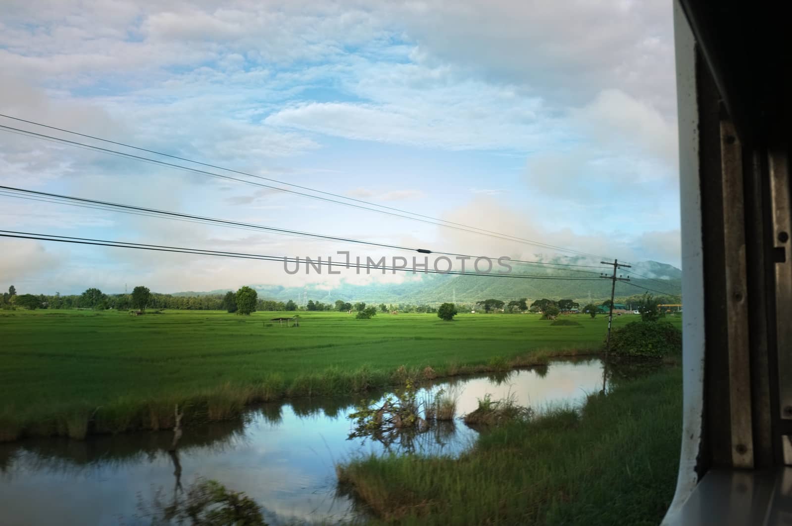 View from train window in motion of countryside and sky on sunny warm , in Thailand , 