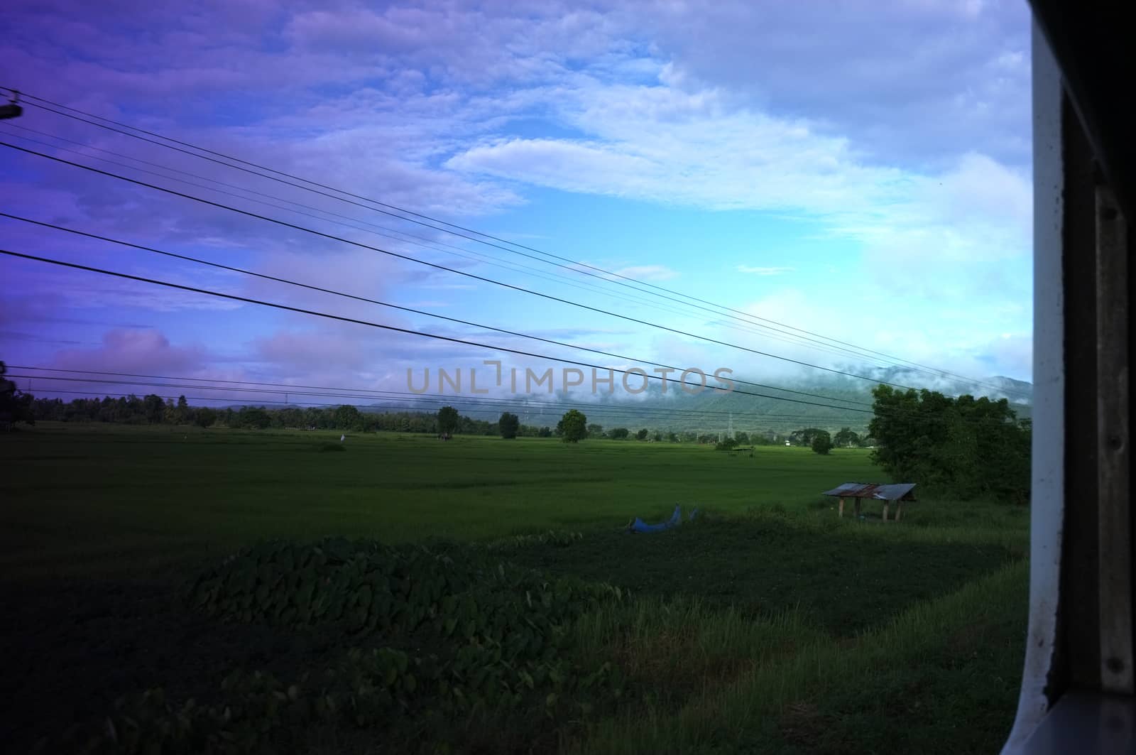 View from train window in motion of countryside and sky on sunny warm , in Thailand , 
