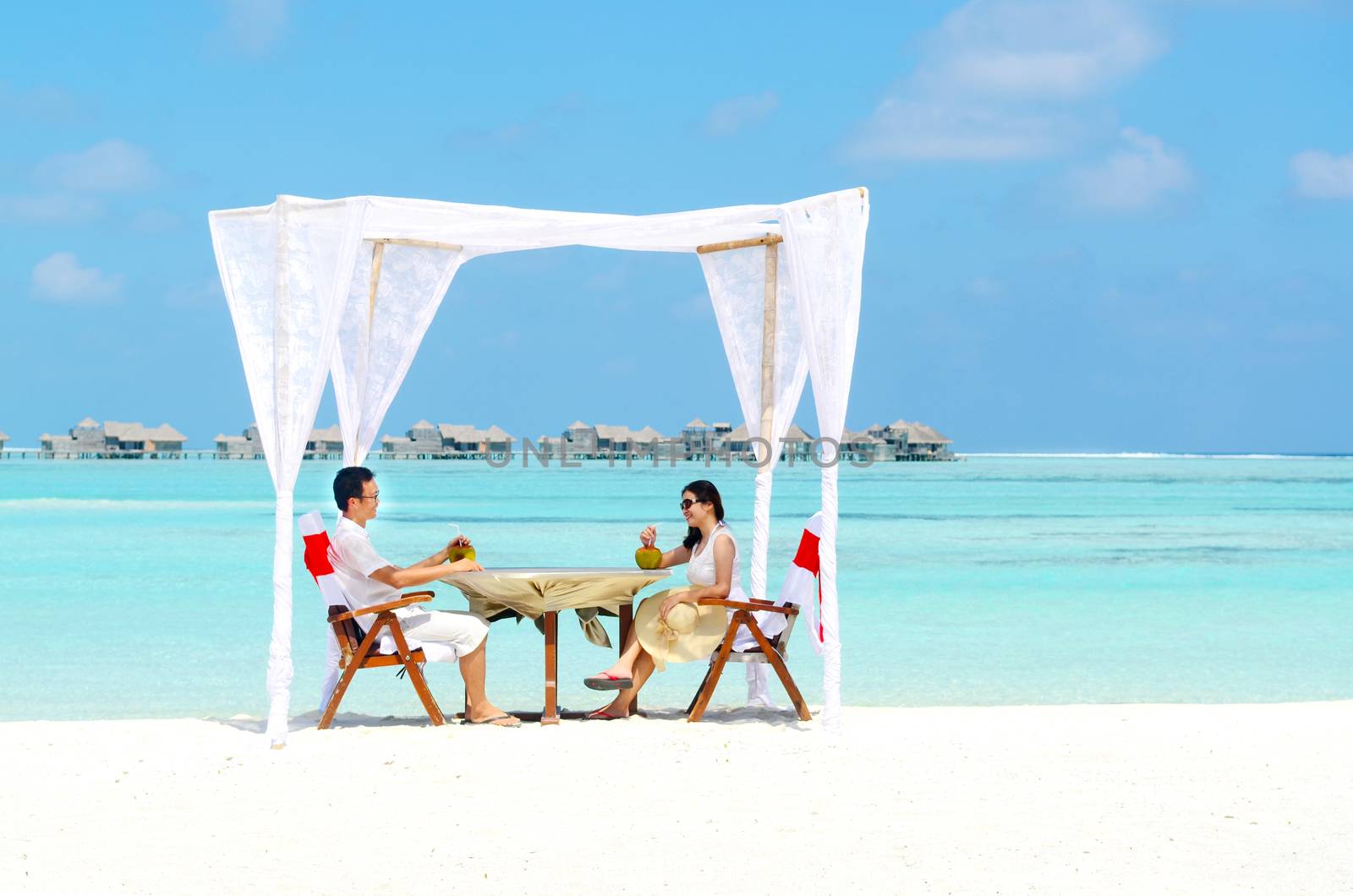 Asian couple enjoying romantic luxury lunch setting at tropical beach in Maldives
