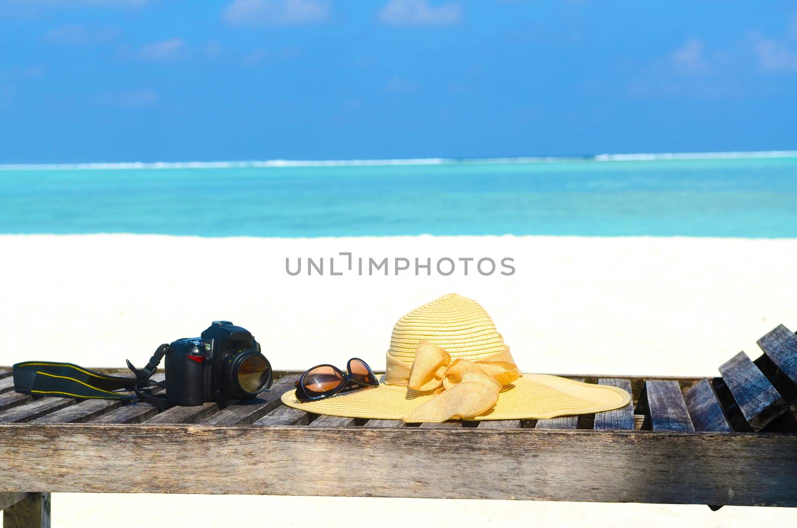 Deckchairs with sunhat, camera and sunglass on jetty in front of tropical resort at maldives island