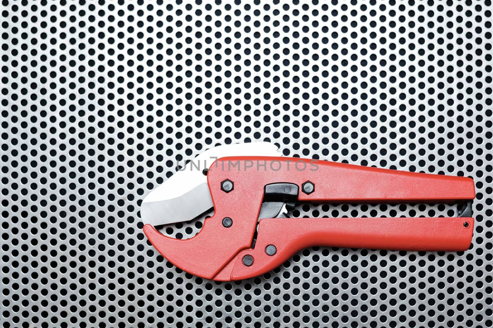 Red scissors for cutting plastic pipe on metal workbench