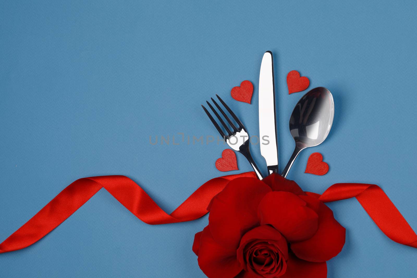 Cutlery set tied with silk ribbon rose flower and hearts on blue background Valentine day dinner concept