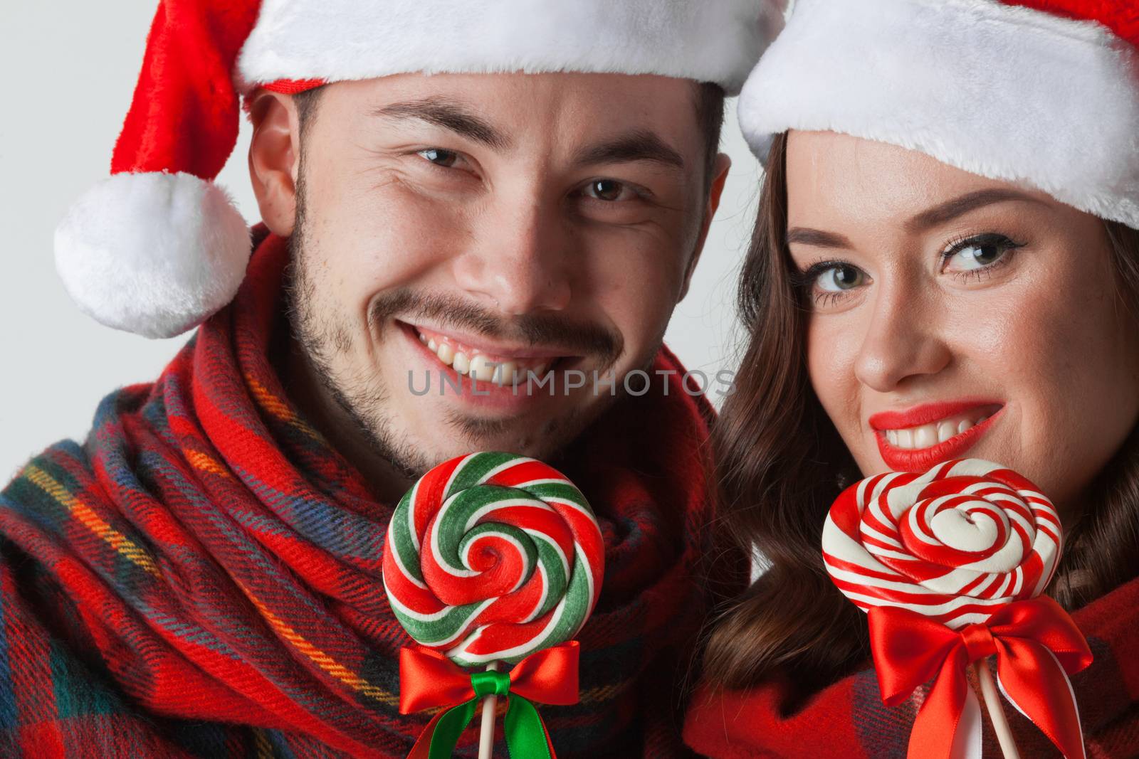 Young happy smiling couple in christmas santa hats with lollipops