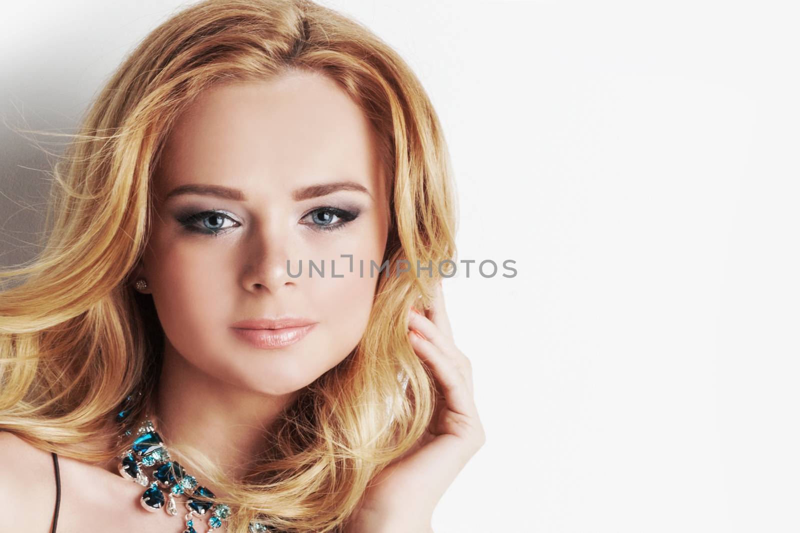 Portrait of beautiful woman with blonde curly hair and necklace of blue precious stones close up