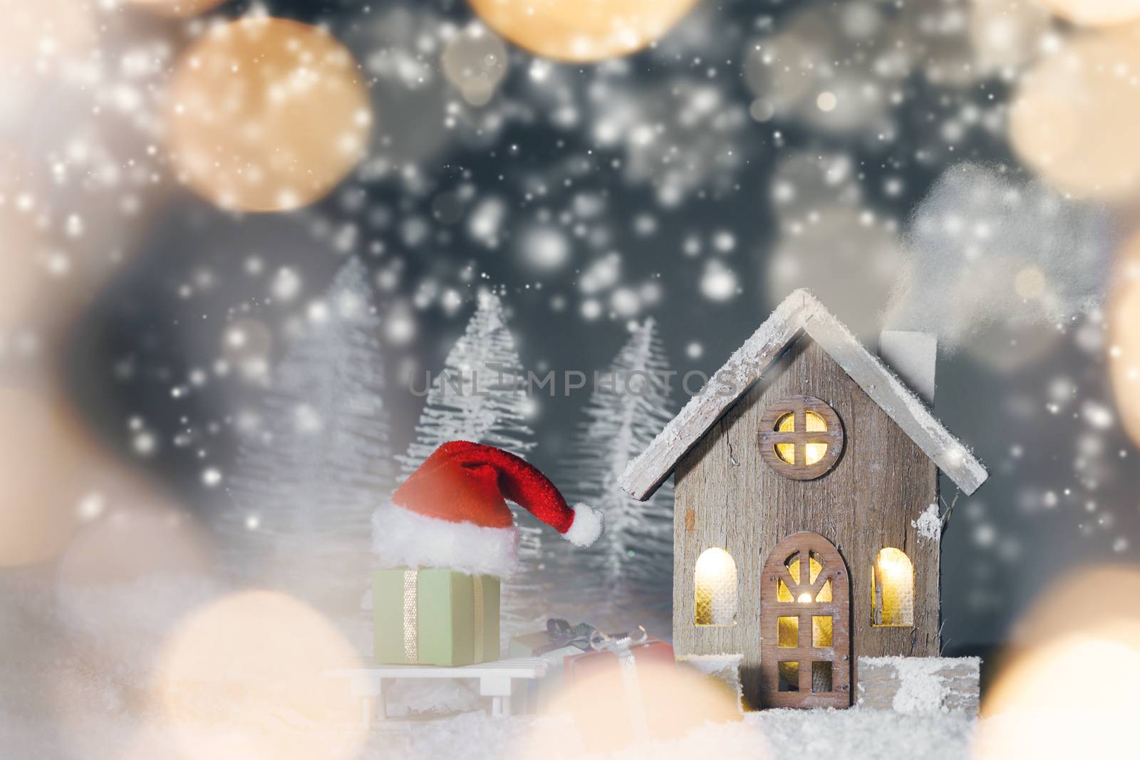 Christmas card with cozy small decorative house , gifts and Santa Claus cap on sleigh on snow over fairy tale winter fir forest background and falling snow . New Year design postcard . Copy space for text