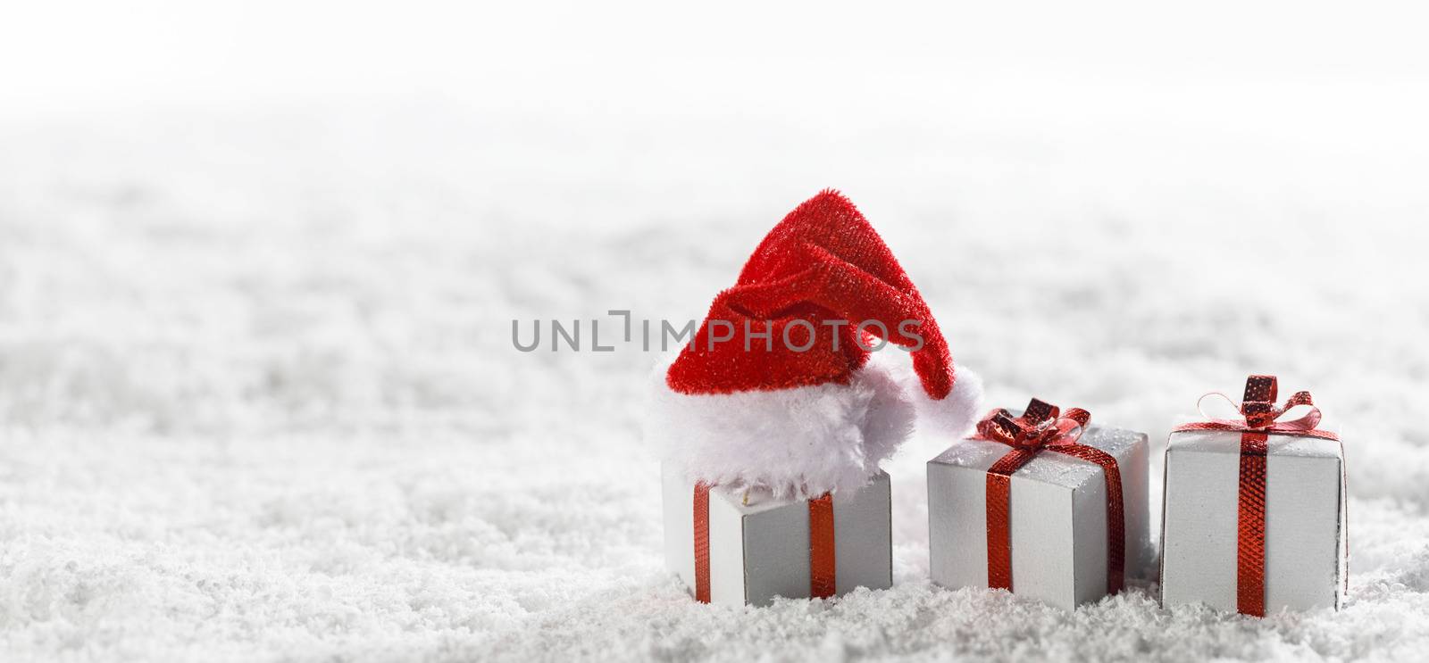 Christmas holidays card with small gifts and santa claus hat in snow