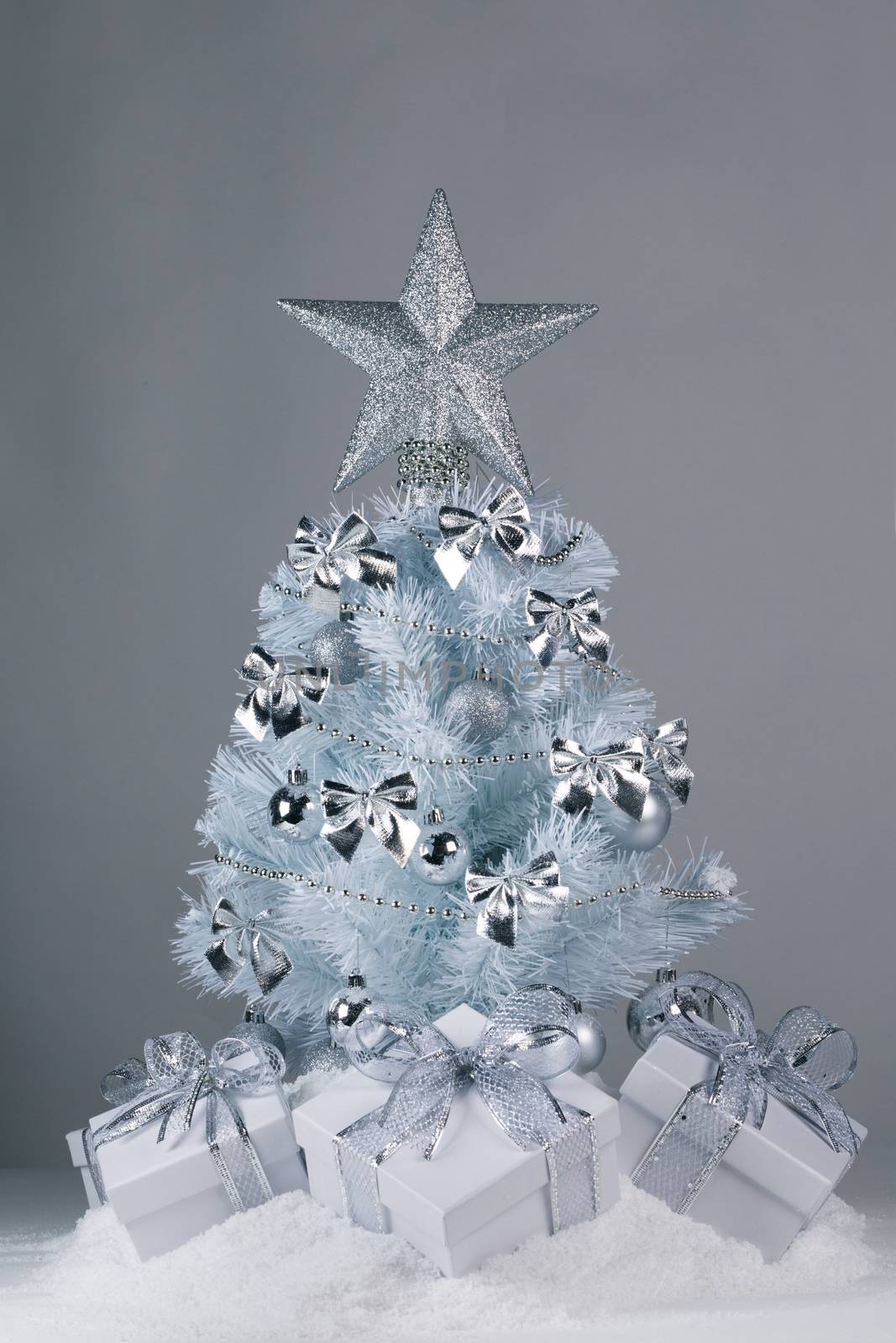 White christmas tree with silver decorations and gifts on snow on gray background