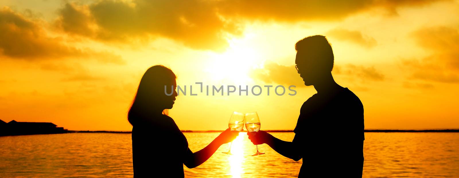 Loving asian couple on the beach, drinking wine at sunset, silhouettes.