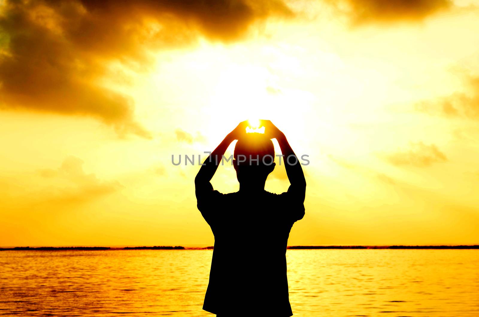 man's hands forming a heart shape with sunset silhouette at tropical beach,maldives island .