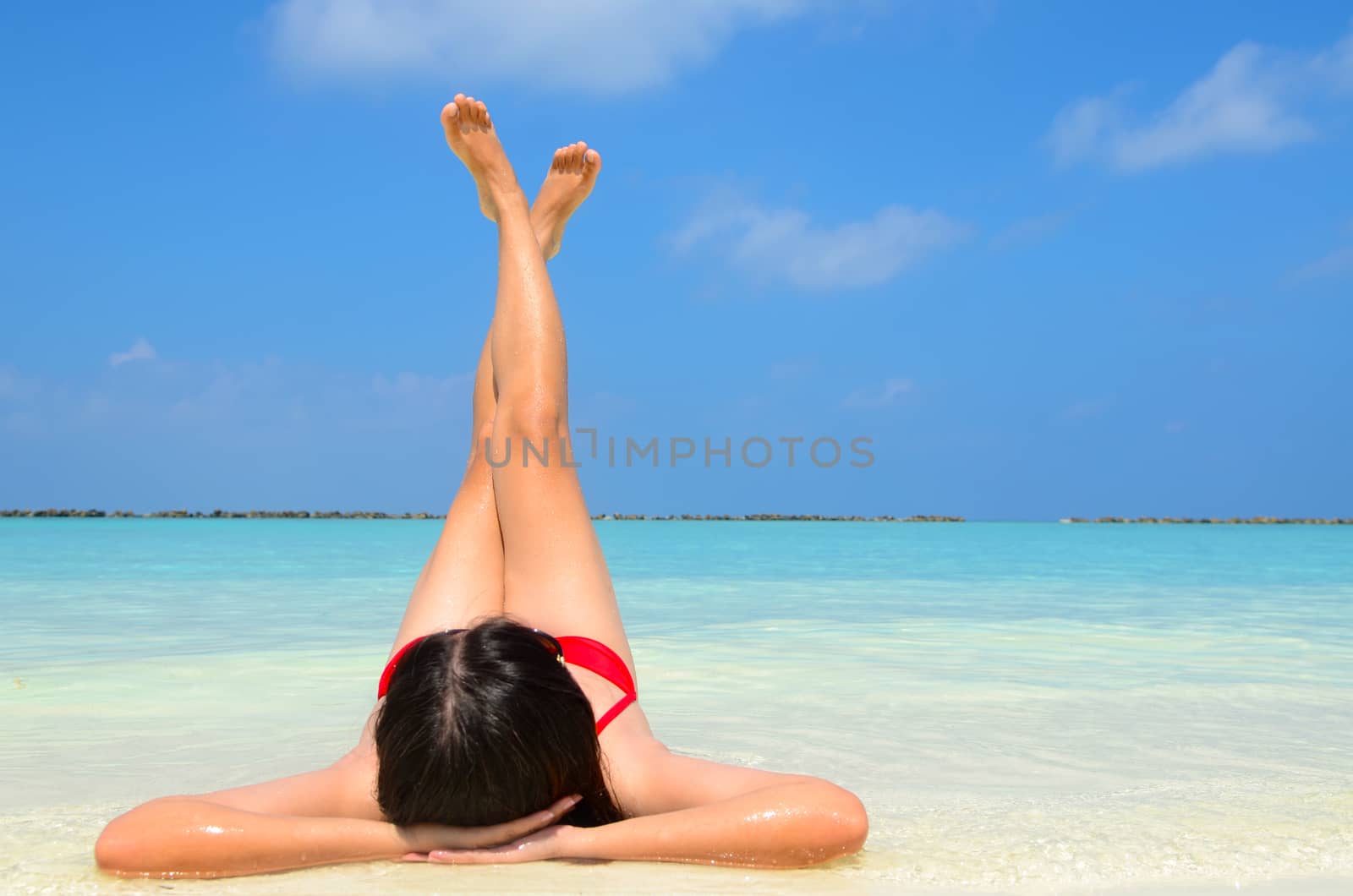 Sexy bikini body asian women enjoy the crystal sea by laying down on white sand of tropical beach and both legs up in the air. Happy island lifestyle. 