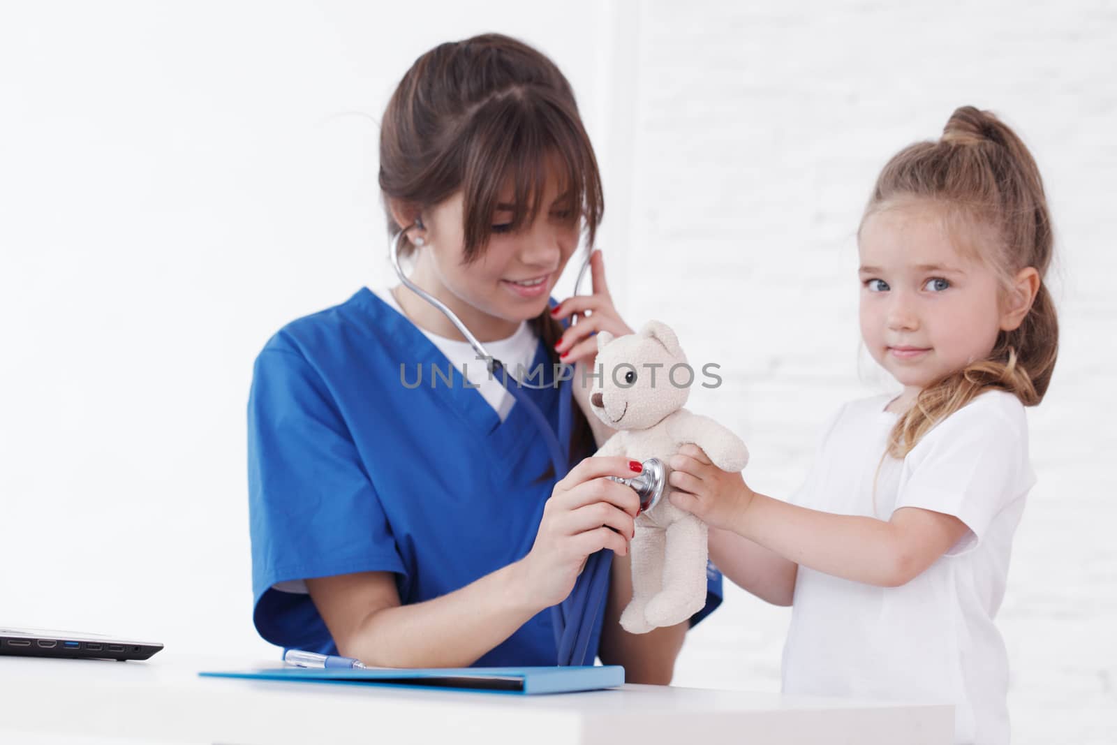 Young smiling female doctor and her little patient with teddy bear