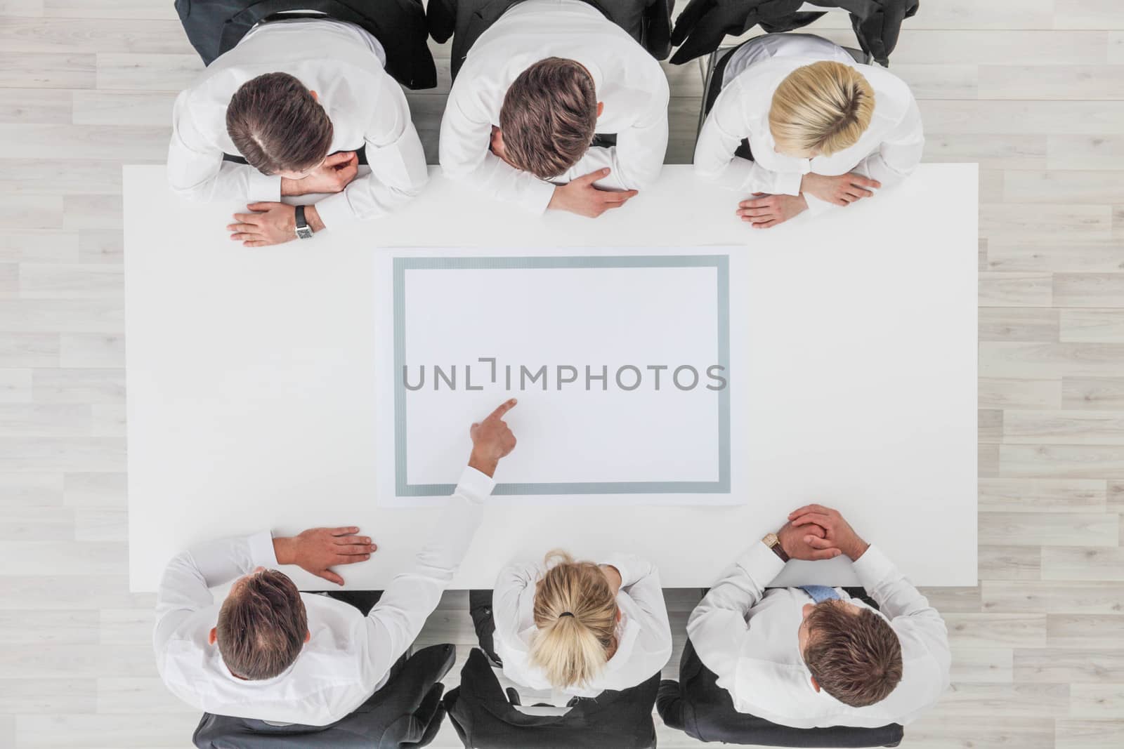Business, people and team work concept - close up of creative team sitting at table and pointing finger to blank copy space for text