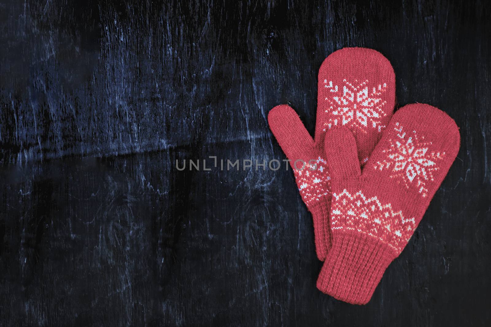 a pair of red-pink-lilac-magenta purple knitted mittens on a dark blue-green-brown wooden vintage background, copy space.