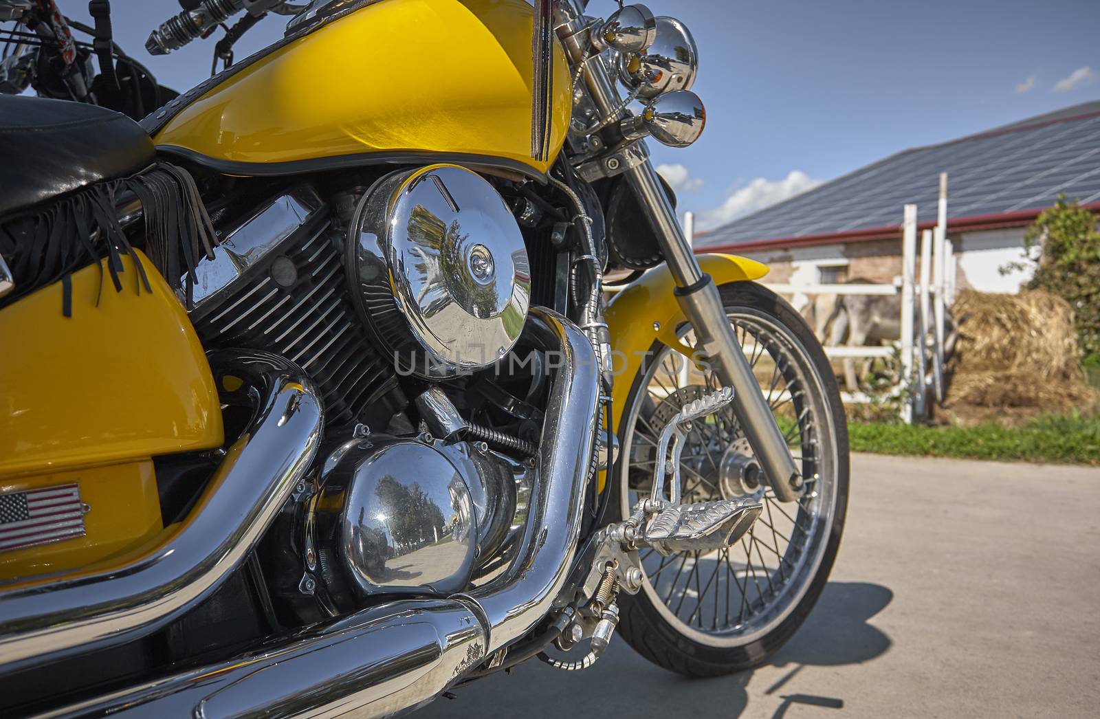 Customized yellow-colored motorcycle with chrome-plated parkings in a countryside landscape during an outdoor voyage.