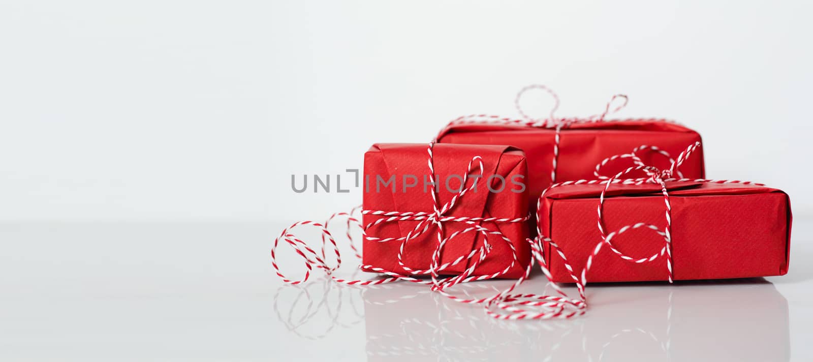 Christmas gift boxes wrapped in red paper and bow of dtriped rope on white background