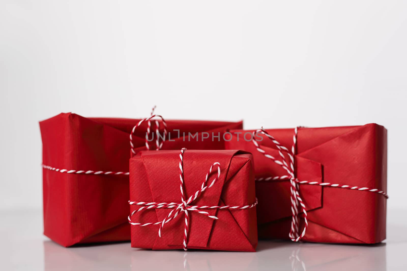 Christmas gift boxes wrapped in red paper and bow of dtriped rope on white background