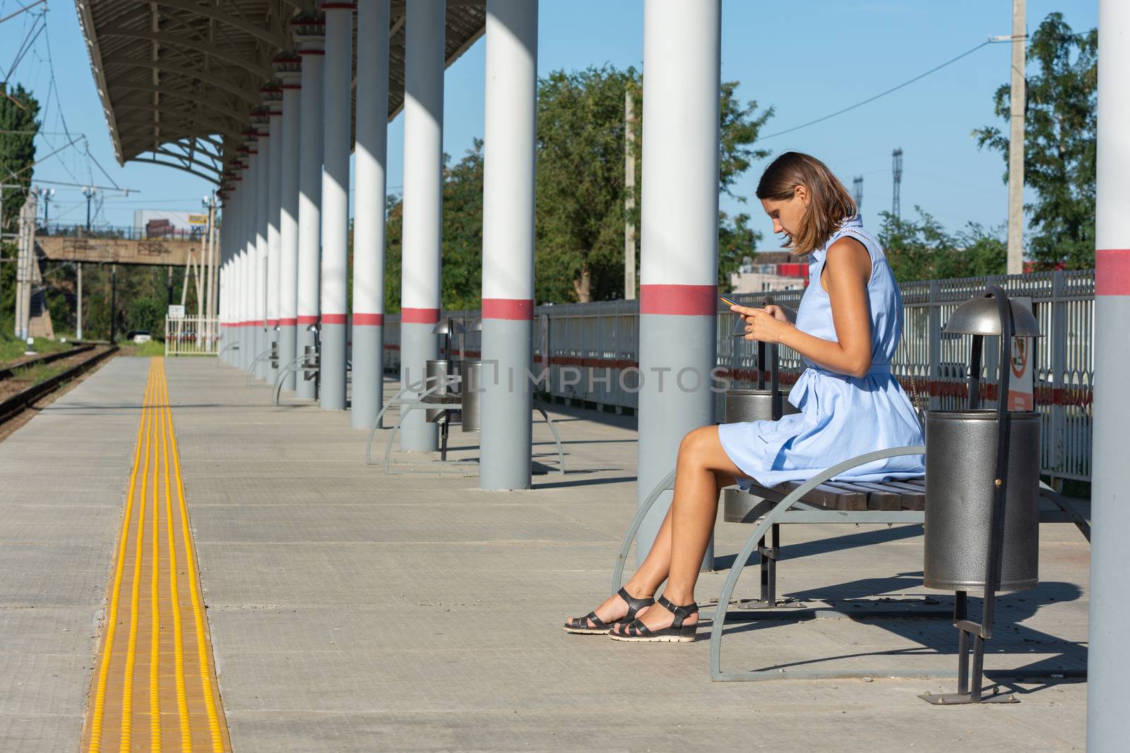 Young girl looks at the phone on the empty platform of the railway station