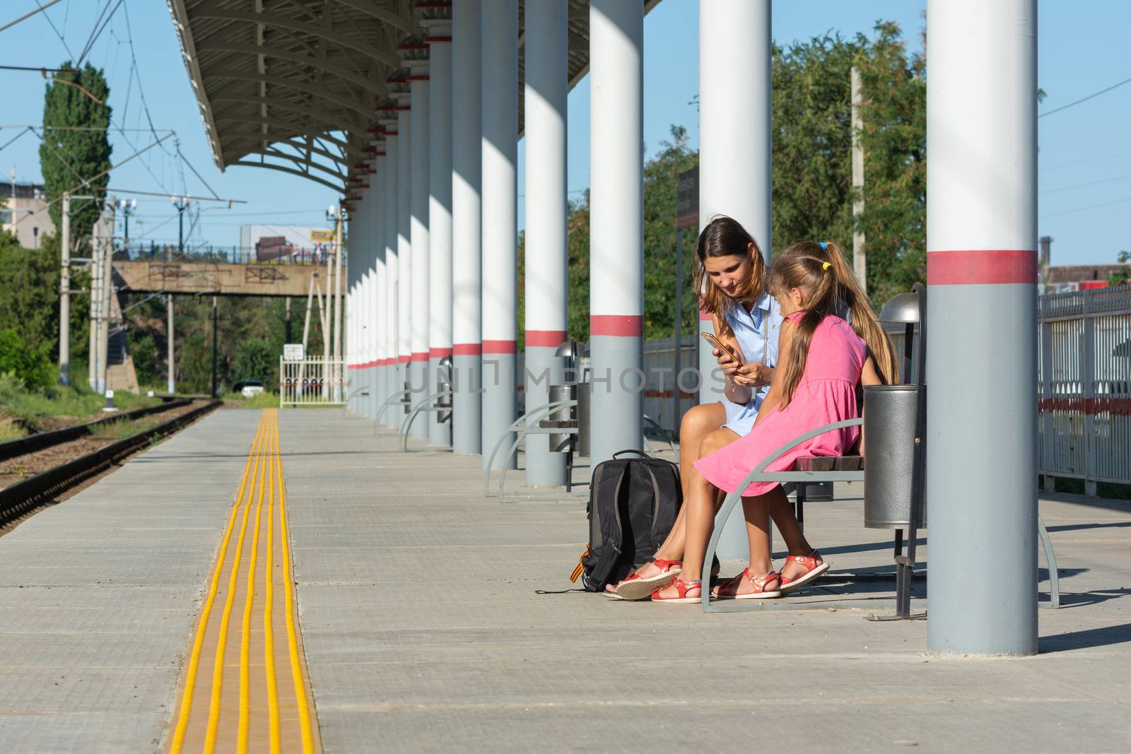 Mom and daughters are waiting for the train on the empty platform of the railway station