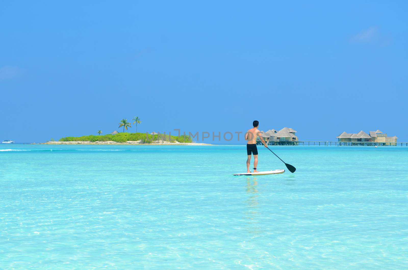 Young asian man paddle board rowing on sunny tropical paradise island with blue  sea water ocean in Maldives island.