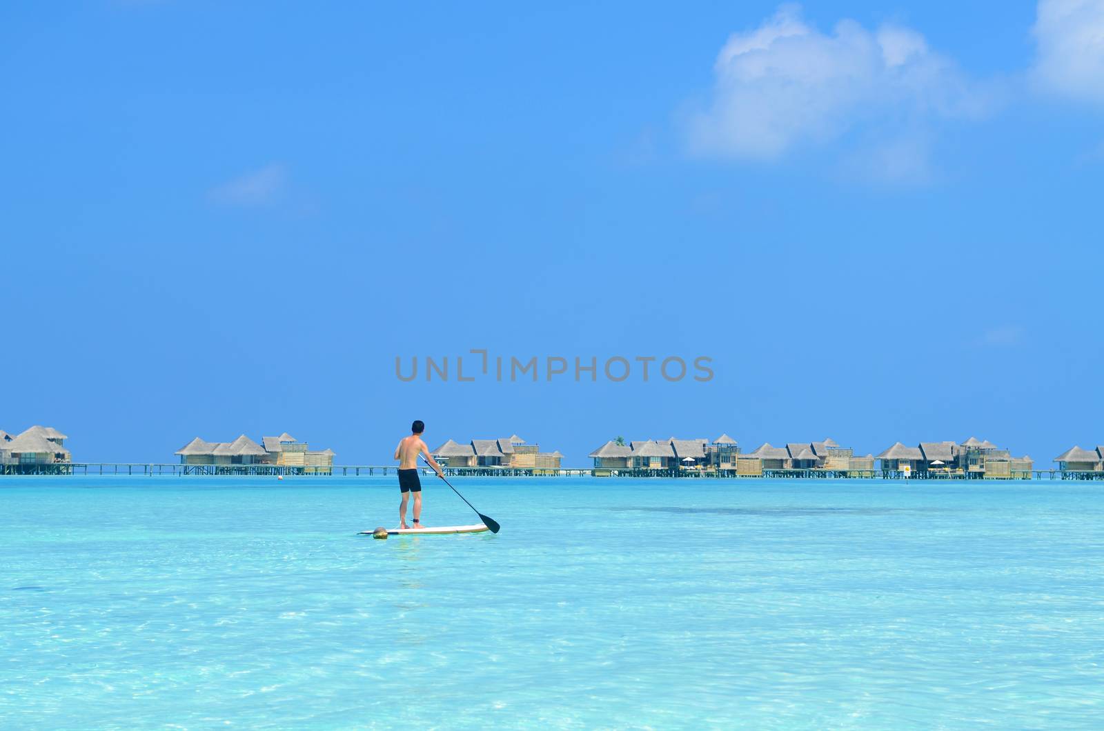 Young asian man paddle board rowing on sunny tropical paradise island with blue  sea water ocean in Maldives island.