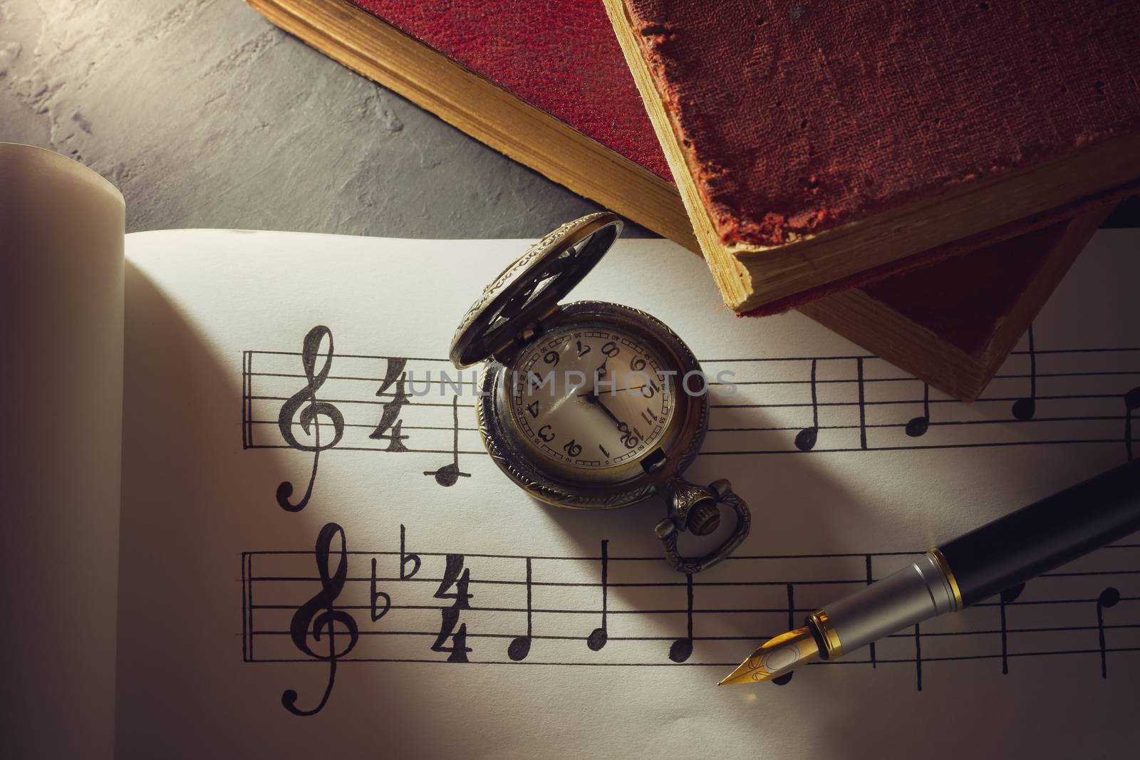 Music notes and old book with pocket watch on wooden table background in morning light. Writing chords by vintage pen. Closeup and copy space for text. Concept of Music lovers.