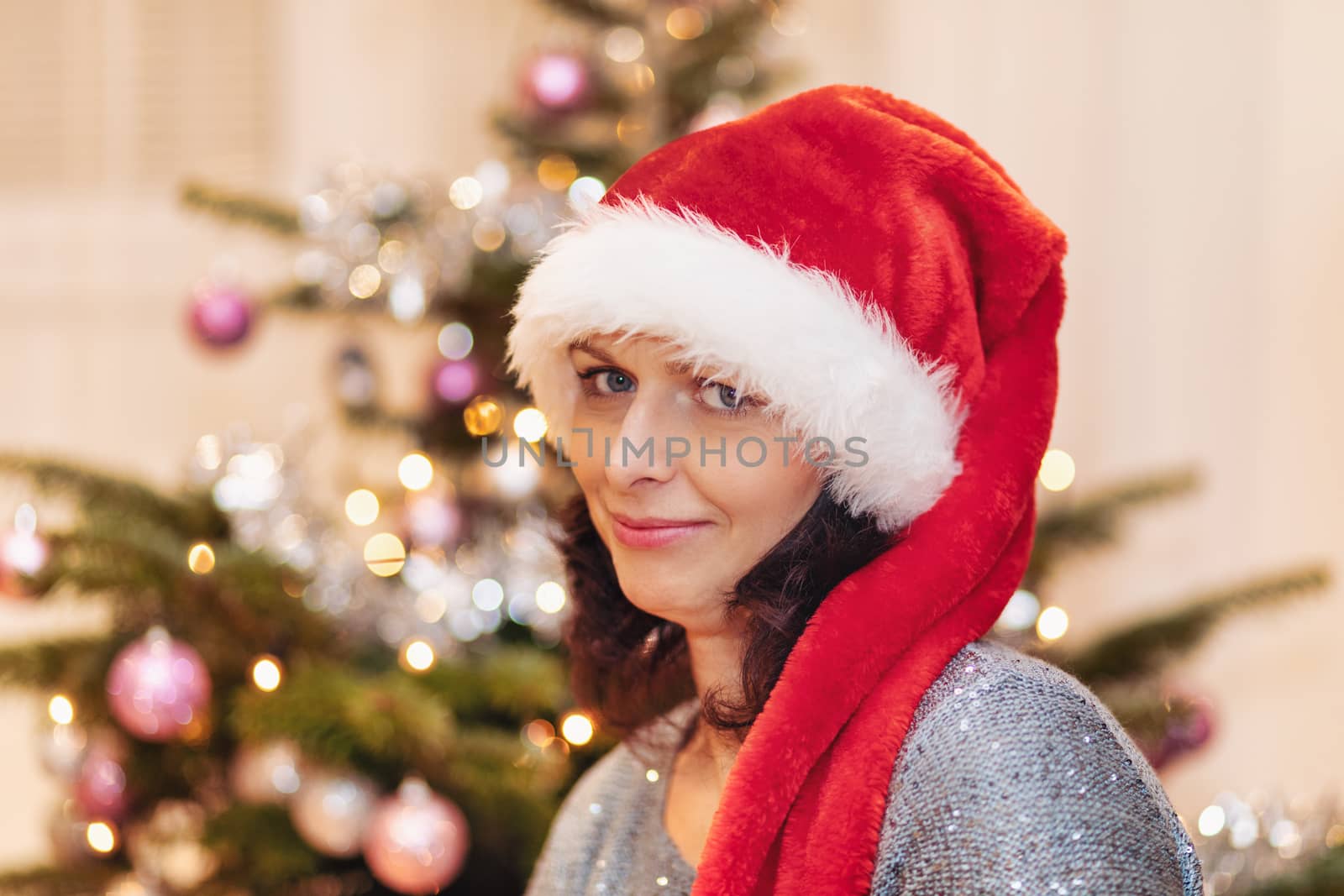 Beautiful middle age woman in santa hat sitting near the Christmas tree by artush