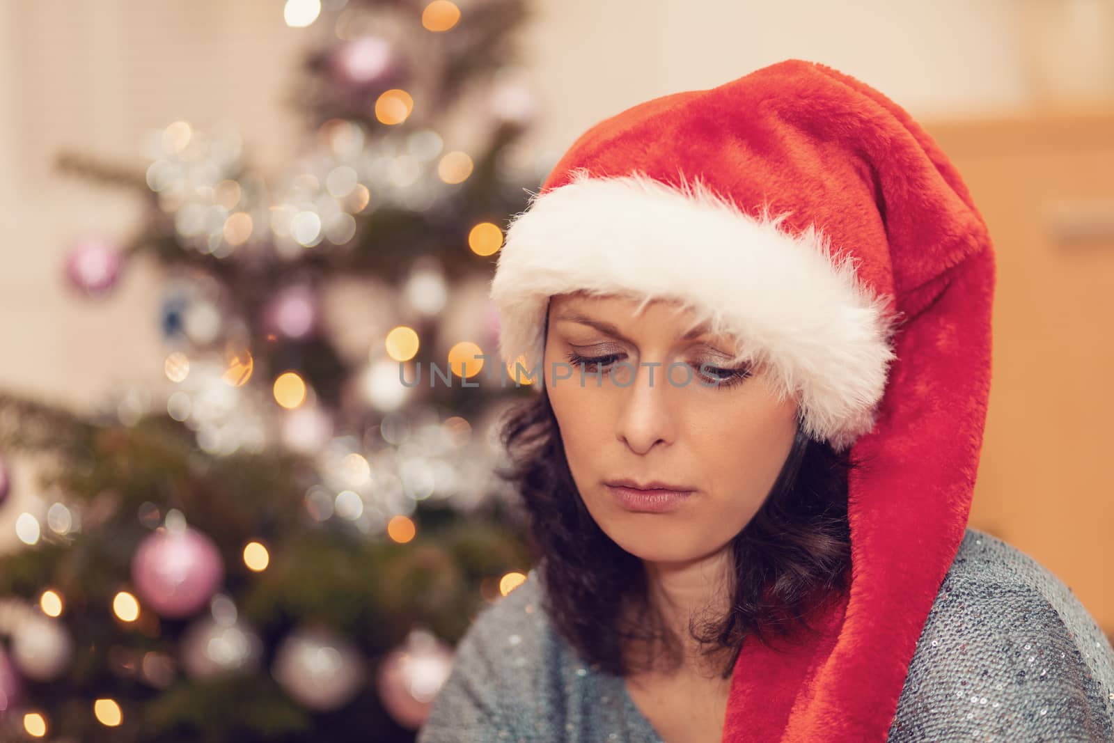 Beautiful middle age woman in santa hat sitting near the Christmas tree by artush